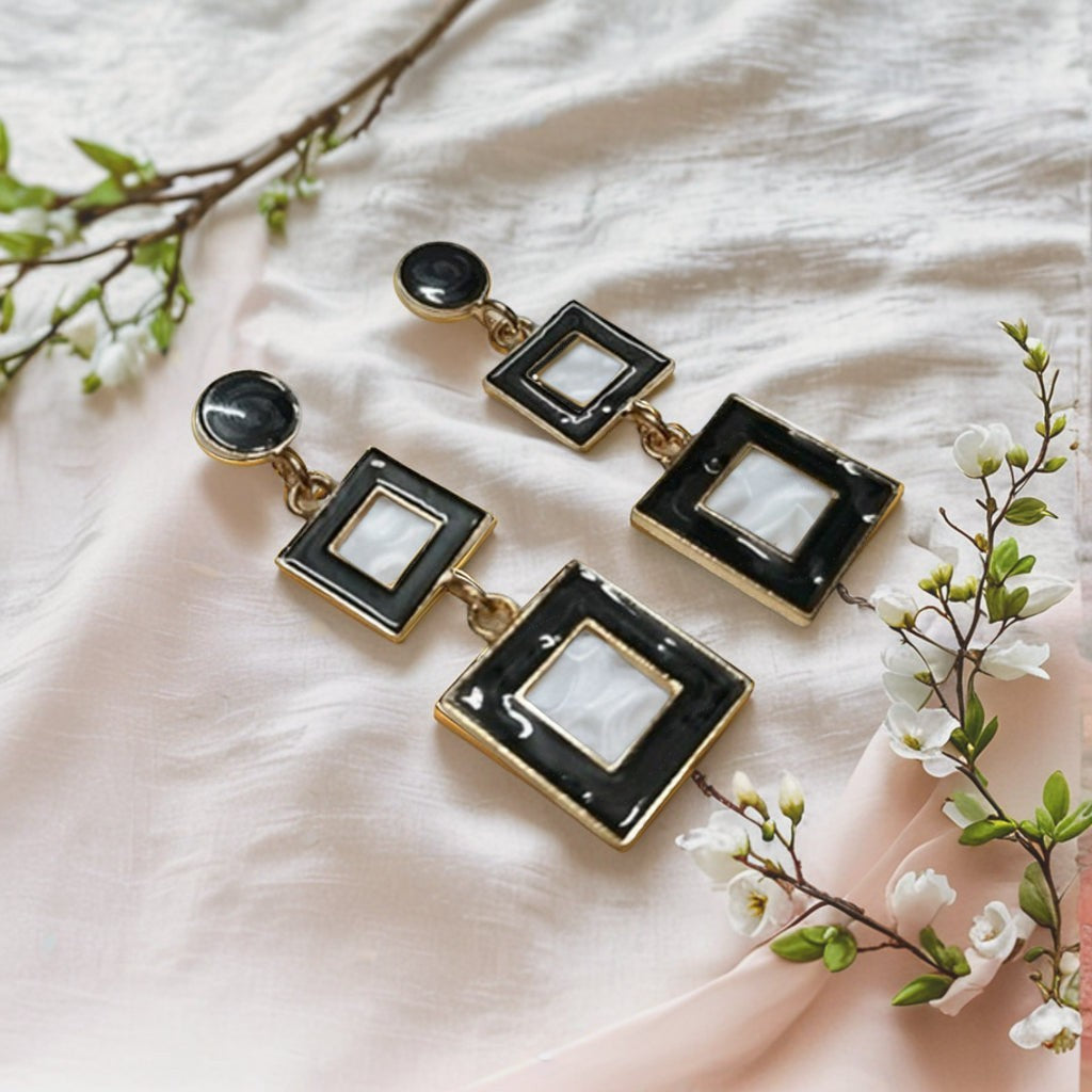 dazzle21 modern geometric square drop earrings featuring black and white enamel detail on a soft fabric background