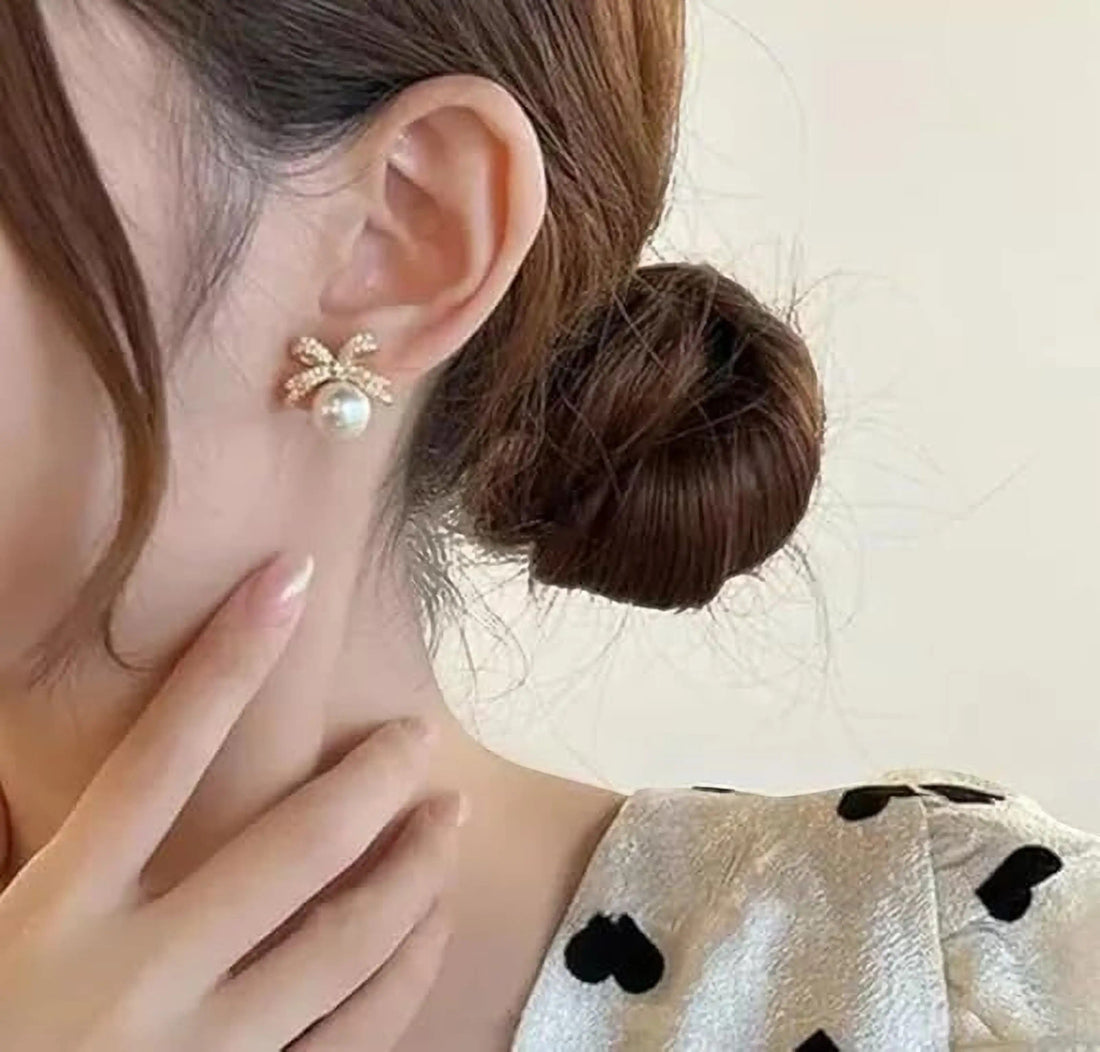 dazzle21 gold plated bow stud earring with a white pearl accent worn on a woman's ear