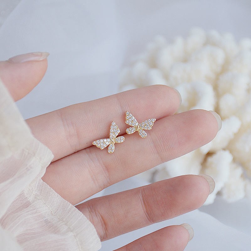 dazzle21 gold-tone butterfly stud earrings embellished with sparkling crystal stones held on fingertips