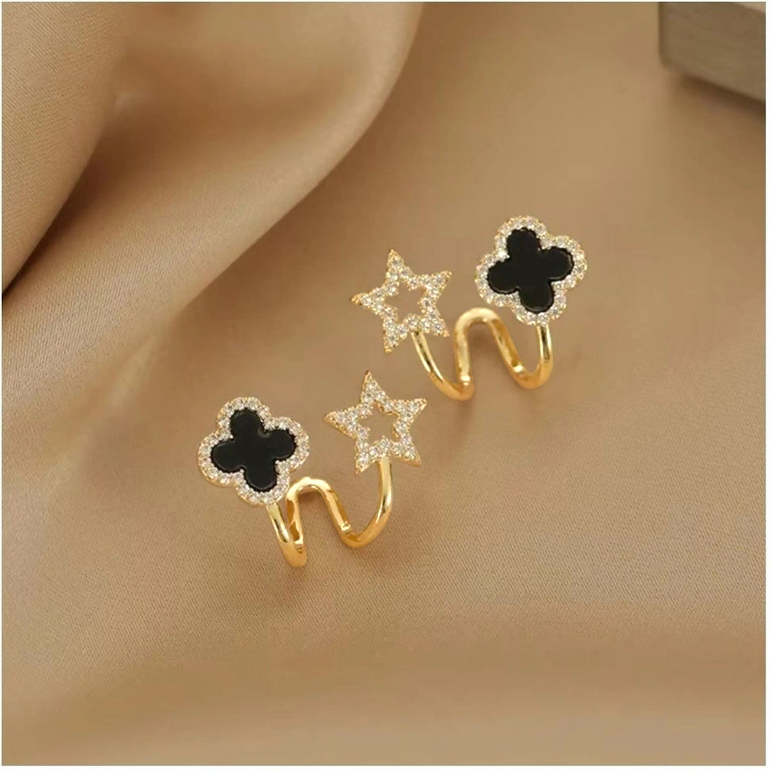 dazzle21 gold-tone ear cuffs featuring black clover and crystal star charms on a soft champagne fabric background