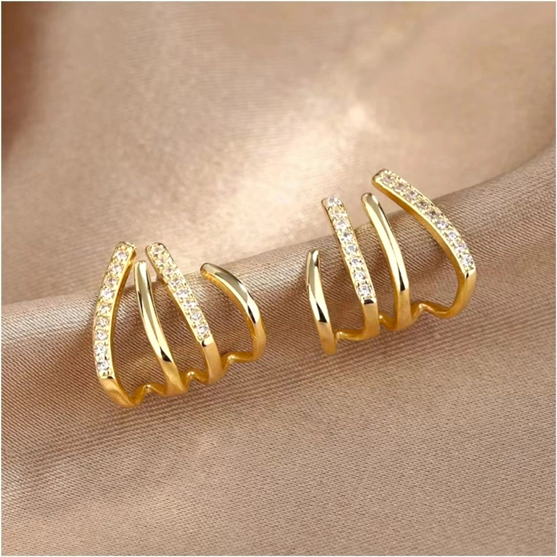 dazzle21 gold-toned triple-band hoop earrings with sparkling cubic zirconia stones on a soft satin fabric background