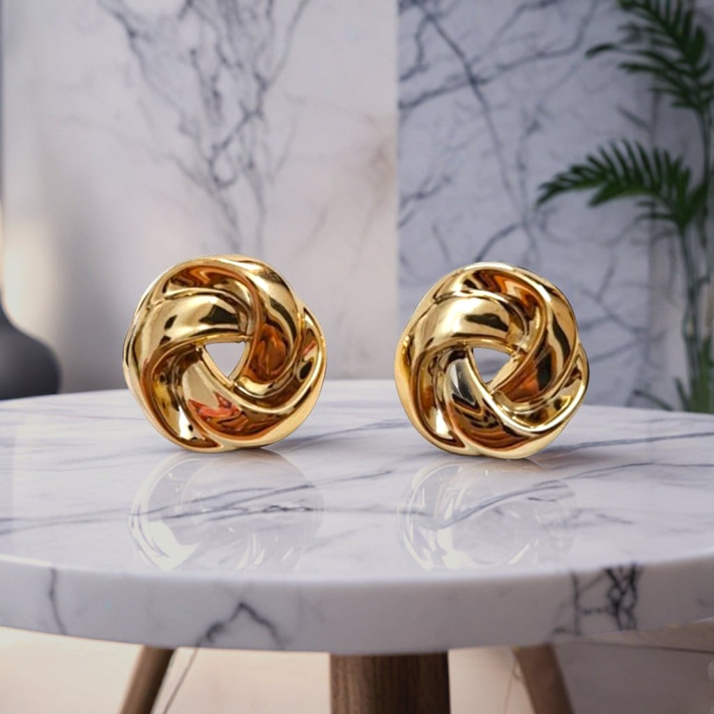 dazzle21 polished gold twisted knot earrings resting on a white marble table with a modern interior background