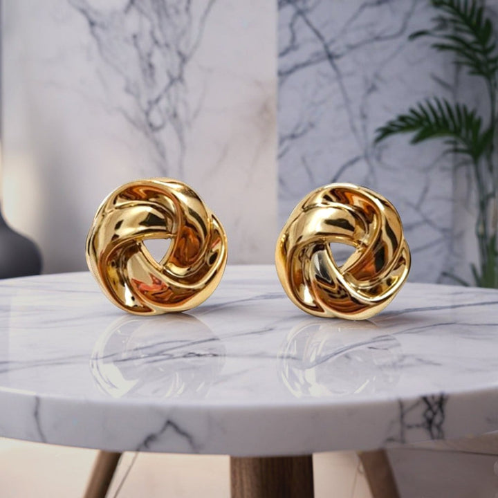 dazzle21 polished gold twisted knot earrings resting on a white marble table with a modern interior background