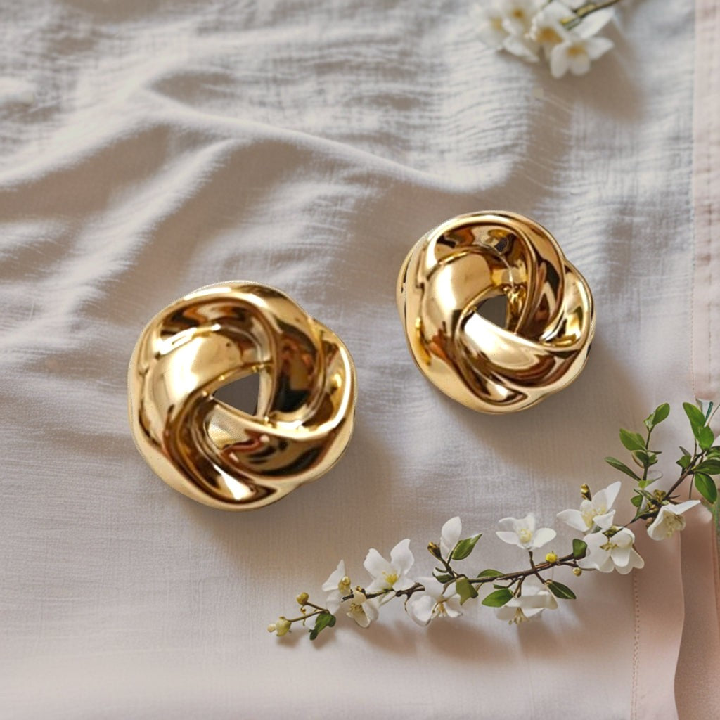dazzle21 polished gold twisted knot earrings resting on a soft beige fabric with small white flowers