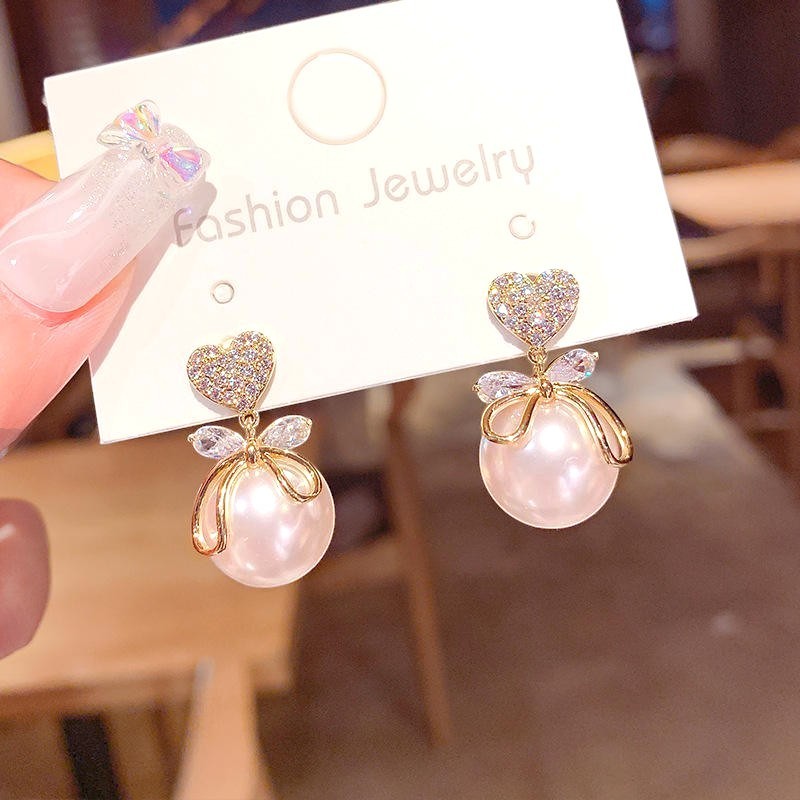 dazzle21 Luxe Heart Pearl Bow Drop Earrings featuring crystal heart studs, gold bows, and lustrous faux pearl drops.