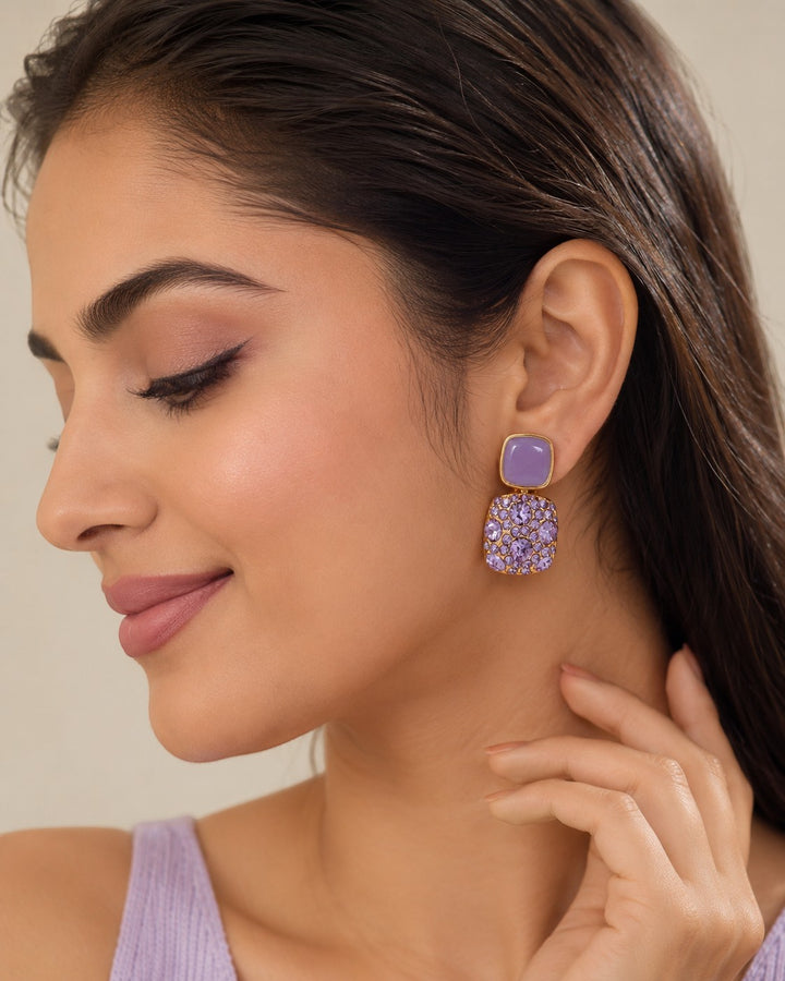 dazzle21 lavender enamel and crystal statement earrings worn by a woman with a soft glam makeup look