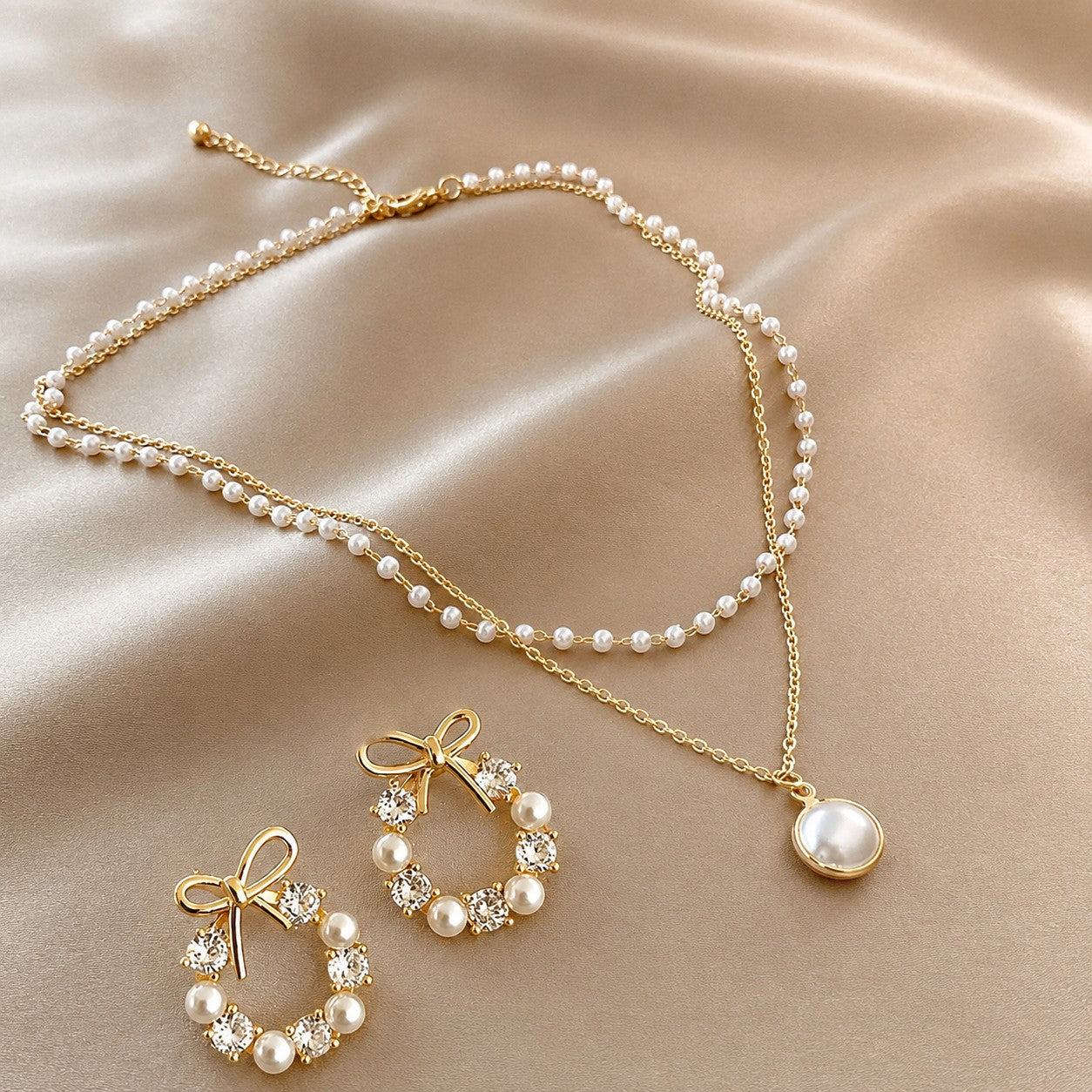 dazzle21 gold-tone jewelry set featuring a double-layer pearl necklace with pendant and bow-shaped crystal pearl earrings