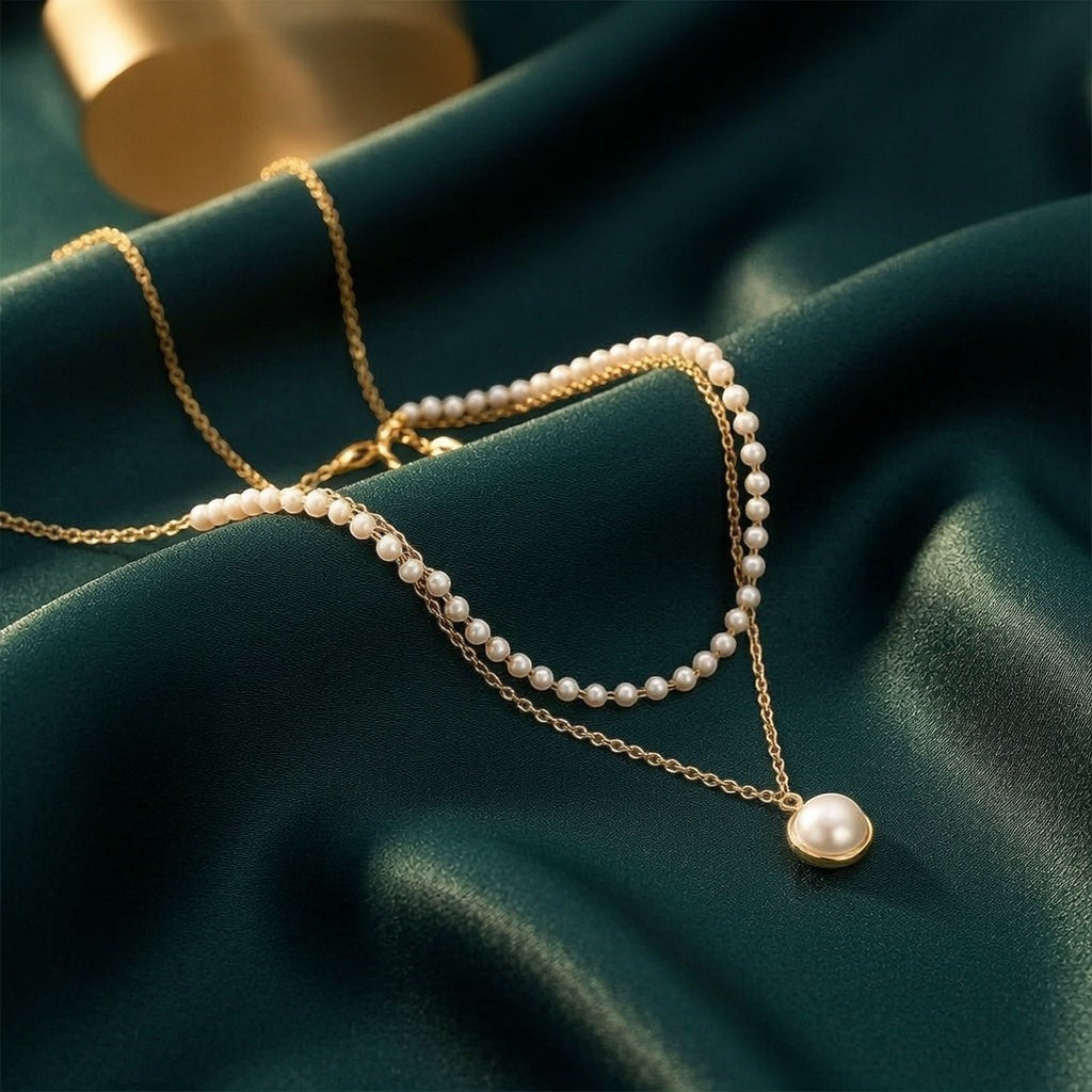dazzle21 layered gold chain necklace with small white pearls and a single pearl pendant on dark green satin fabric