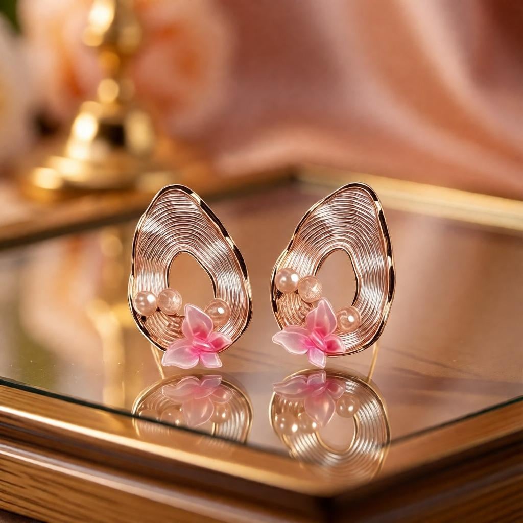dazzle21 pear-shaped ribbed gold earrings with pink butterfly accents and pearl details on a reflective surface