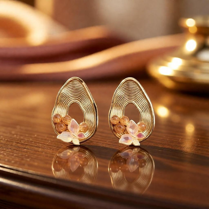 dazzle21 pear-shaped gold ribbed earrings with butterfly and pearl accents on a reflective surface