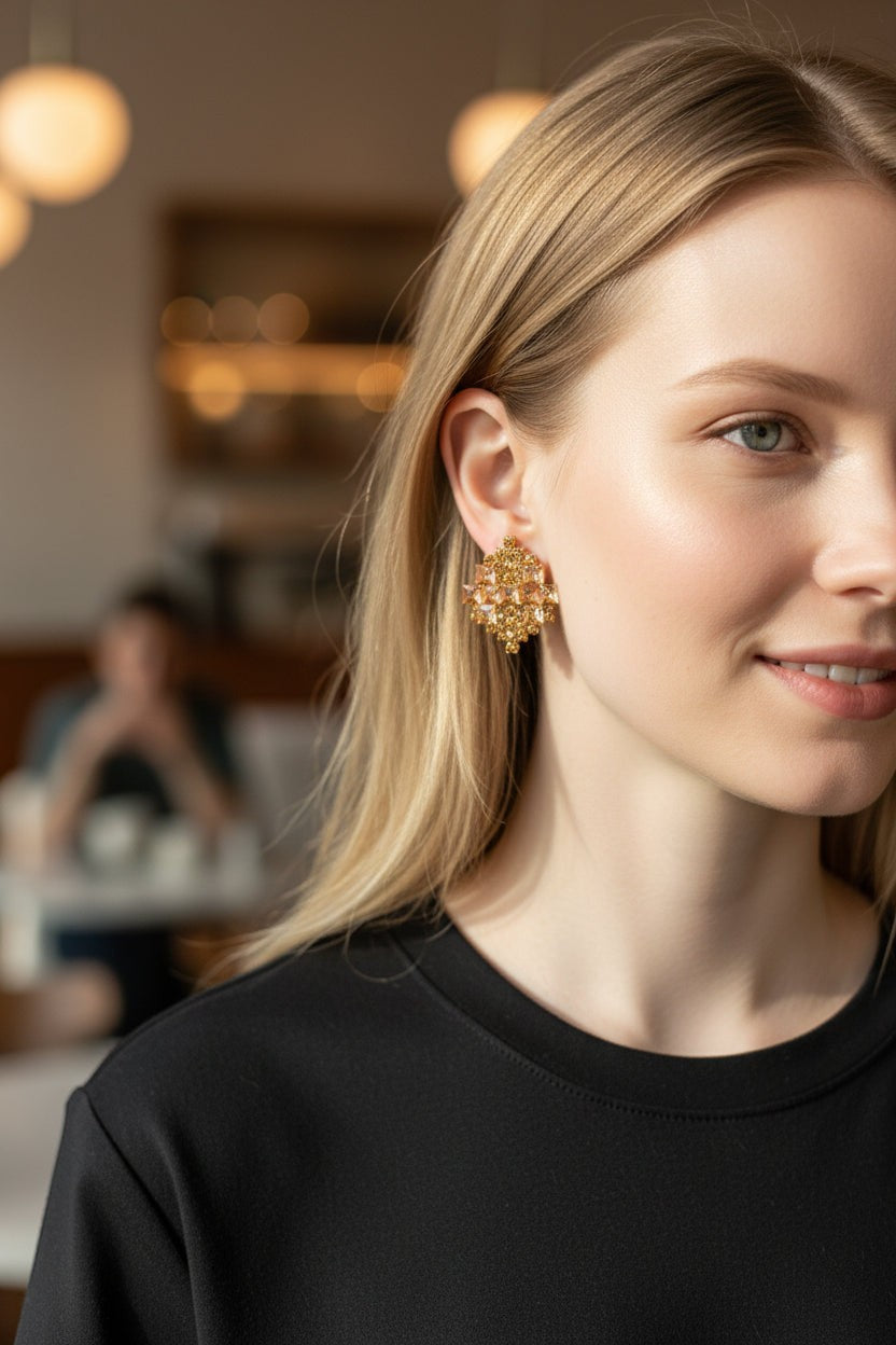 dazzle21 geometric crystal stud earrings in rose gold worn by a blonde woman in a soft-focus cafe setting