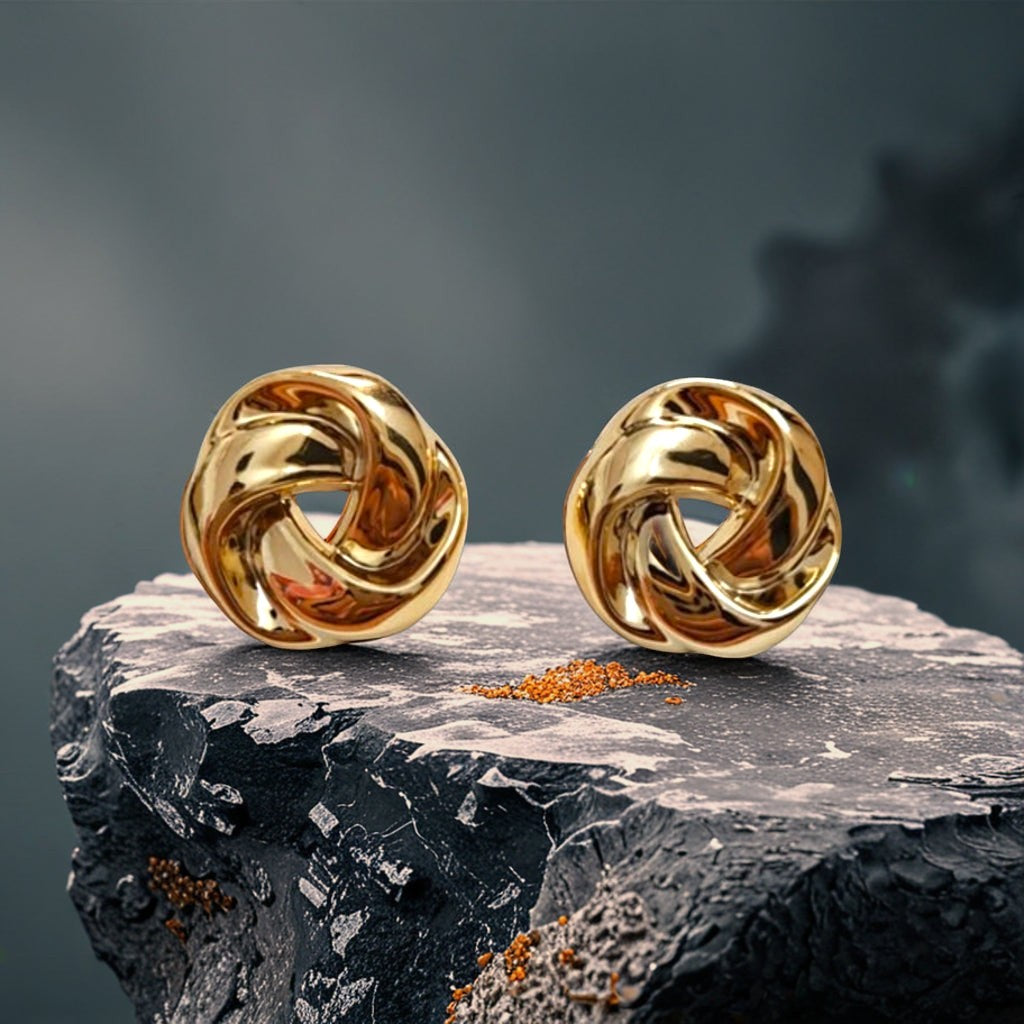dazzle21 twisted knot earrings in polished gold finish displayed on a textured dark stone surface.